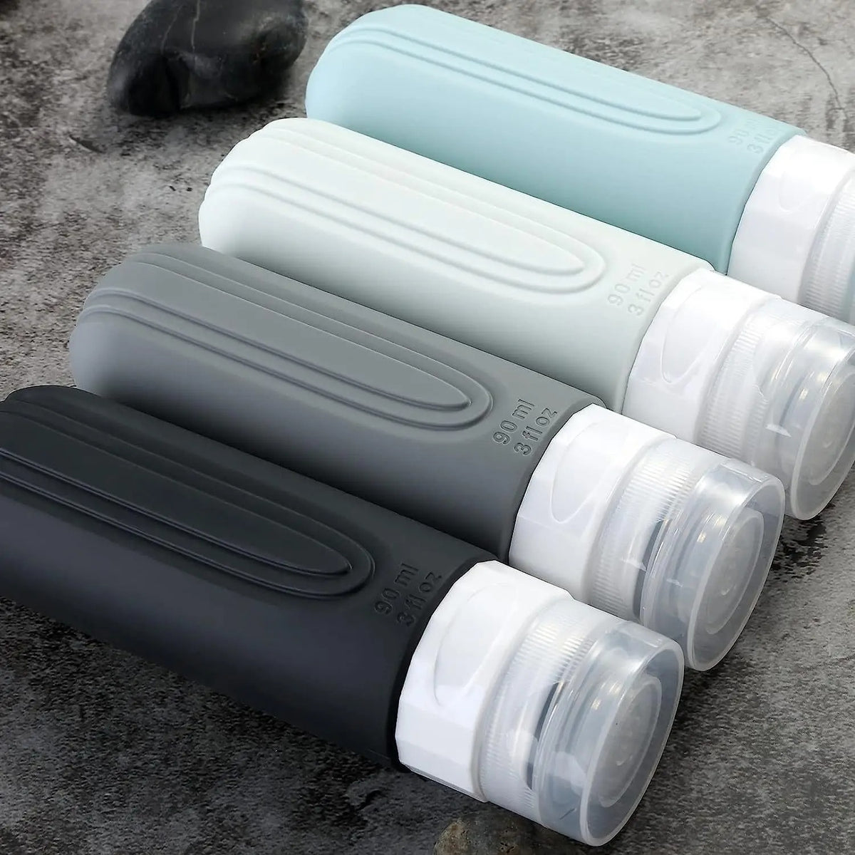 4 flacon voyage antifuite gris posé sur le sol de la salle de bain