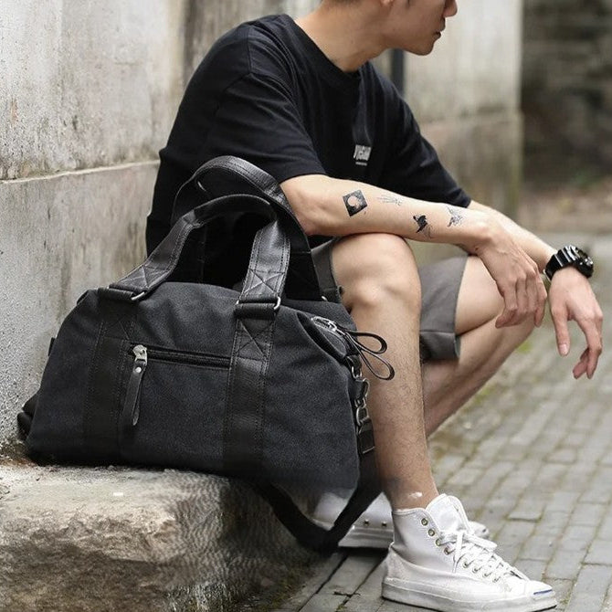 homme posé à coté d'un sac week end pour homme en toile vintage noir